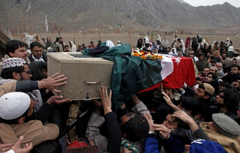 Relatives and neighbors reach out to carry the coffin of a police officer who was killed with others by a bomb blast in a mosque, during a funeral in Quetta