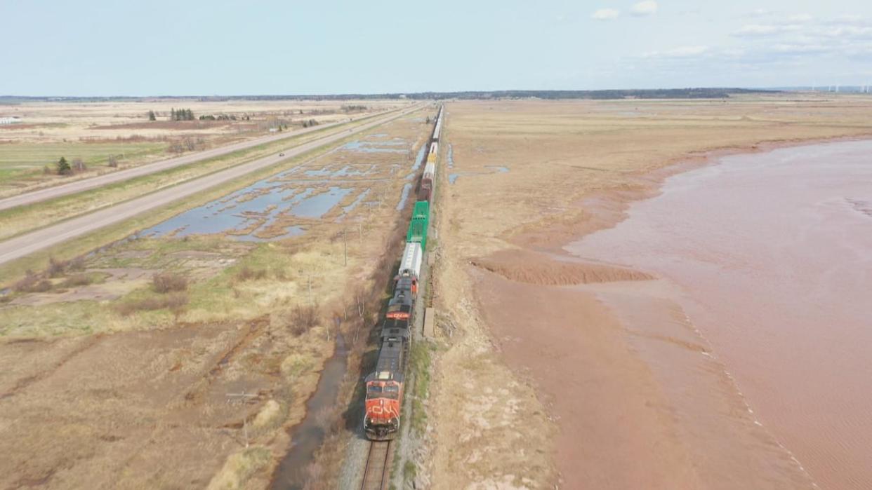 A freight train moves along the CN rail line over the Chignecto Isthmus with the four-lane Trans-Canada Highway on the left.  (Shane Fowler/CBC - image credit)