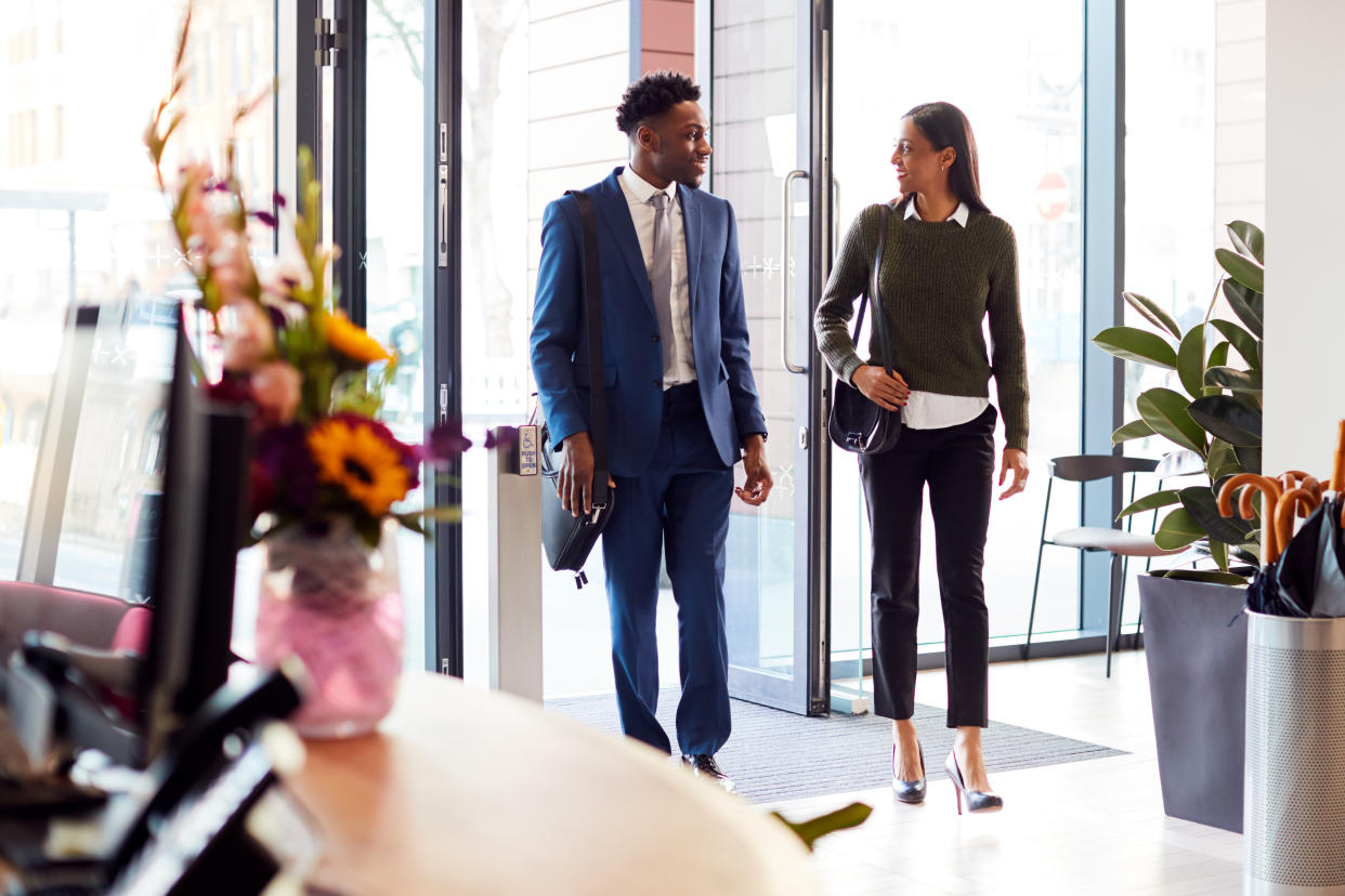 Businessman And Businesswoman Arriving For Work At Office Walking Through Door