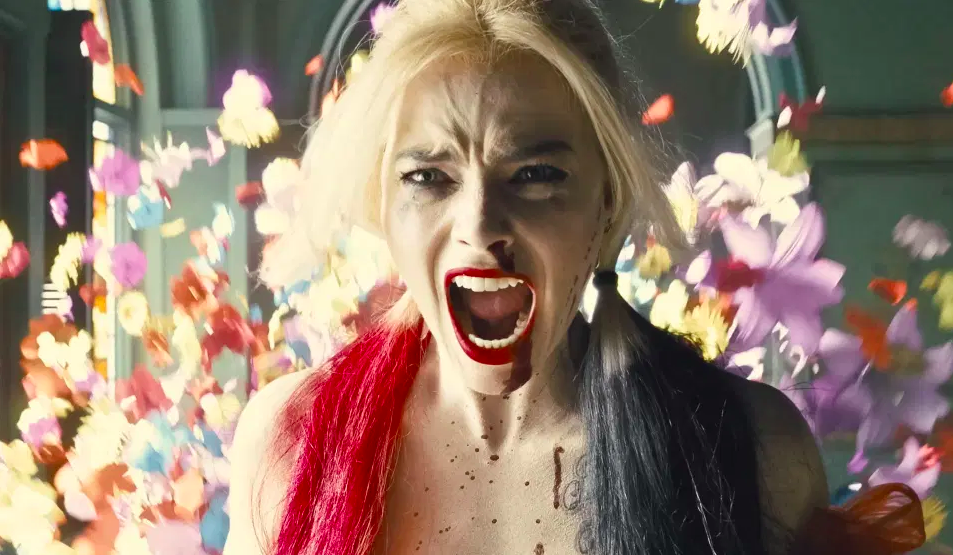 A still from The Suicide Squad shows Harley Quinn with flowers exploding behind her