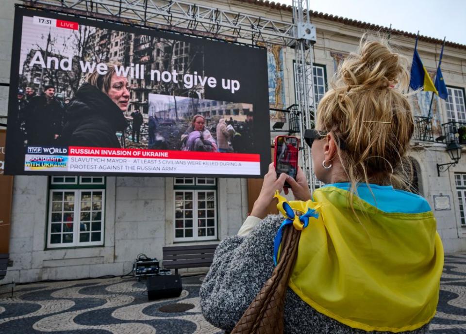 cascais, portugal   march 27 a woman wrapped in a ukrainian flag, takes a picture of a giant screen that says and we will not give up while standing outside of city hall to watch the international charity tv marathon in support of ukraine save ukraine — stopwar transmitted from warsaw, poland, on march 27, 2022, in cascais, portugal more than 50 celebrities, including fatboy slim, bastille, salvador sobral, netta, jamala, tina karol, julia sanina and sting, performed and delivered their video statements to the audience to draw the attention of the world regarding the war being waged by the russian federation against ukraine and to raise funds to solve the biggest humanitarian problems caused by the military invasion cascais municipality is actively participating in the reception and aid to refugees since russias ground forces invaded ukraine from several directions on february 24 within hours of president vladimir putin announcing his decision to launch an assault portugal has declared its solidarity with ukraine and portuguese president marcelo rebelo de sousa stated his condemnation to russias overt and flagrant violation of international law photo by horacio villaloboscorbiscorbis via getty images