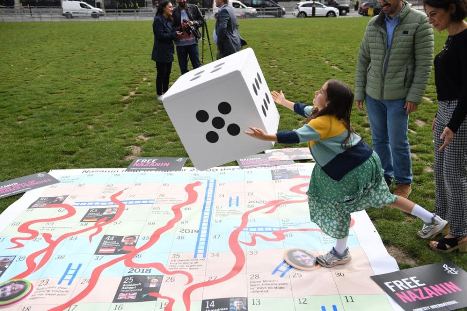 Gabriella Ratcliffe rolls a dice to play on a giant snakes and ladders board in Parliament Square, London to mark the 2,000th day of her mother’s detention in Iran (AFP via Getty Images)