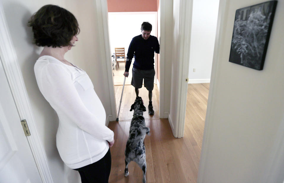 ADVANCE FOR WEEKEND USE APRIL 4-5 -- In this March 14, 2014 photo, Jeff Bauman, talks to his dog Bandit as his fiancee Erin Hurley watches at their Carlisle, Mass., home. Bauman, who lost both his legs above the knee in the Boston Marathon bombing, is learning to adjust to his prosthetics. It takes more energy to walk with prosthetics, which means he gets tired more easily. (AP Photo/Charles Krupa)