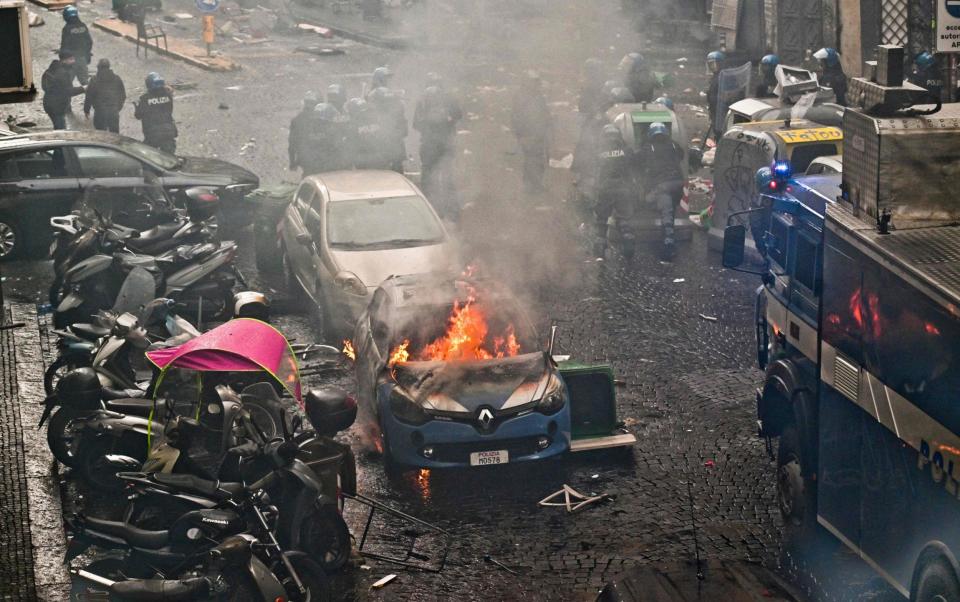 This photo obtained from Italian news agency Ansa shows a police car (Front) burn as Eintracht Frankfurt fans (not in picture) clash with police on March 15, 2023 in downtown Naples prior to the UEFA Champions League round of 16, second leg football match between SSC Napoli and Eintracht Frankfurt - AFP/Ciro Fusco