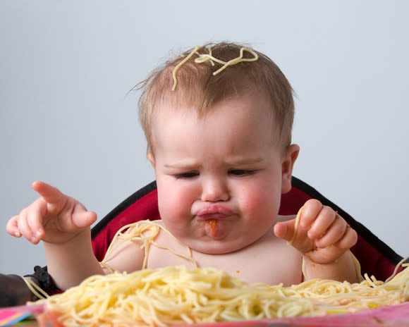 Baby frowning at spaghetti on a high-chair tray