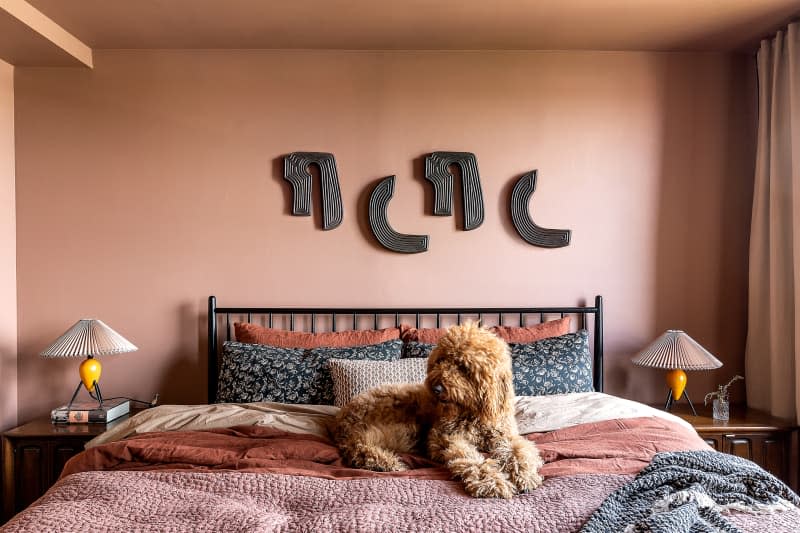 Dog laying on neatly made bed in dusty pink bedroom.
