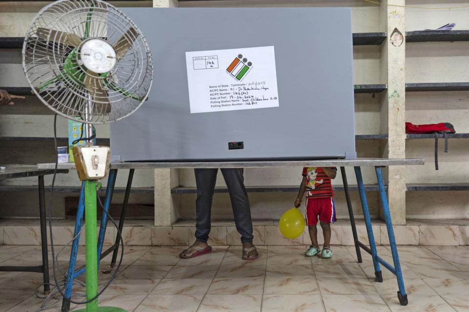 A child holding a balloon stands next to an adult casting his vote at a polling station during the first round of a national election, in Chennai, India, April 19, 2024. (AP Photo/Altaf Qadri)