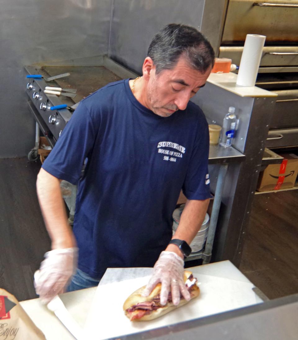 Carlos Catalan of the Supreme House of Pizza puts the finishing touches on a sandwich for a customer during a busy period on Tuesday, Nov. 14, 2023.