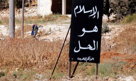 A Syrian army soldier holds a Syrian flag as he stands on a military vehicle in Khan Sheikhoun, Idlib