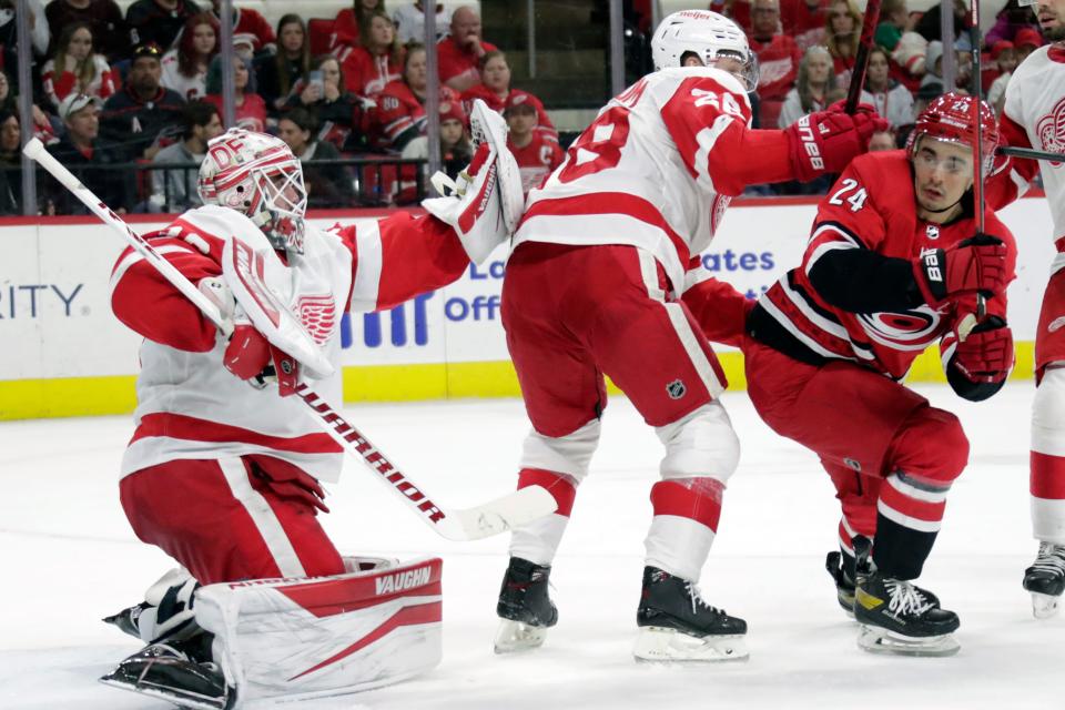 Red Wings goaltender Alex Nedeljkovic gloves a shot while defenseman Gustav Lindstrom guards Hurricanes center Seth Jarvis during the second period on Thursday, April 14, 2022, in Raleigh, North Carolina.