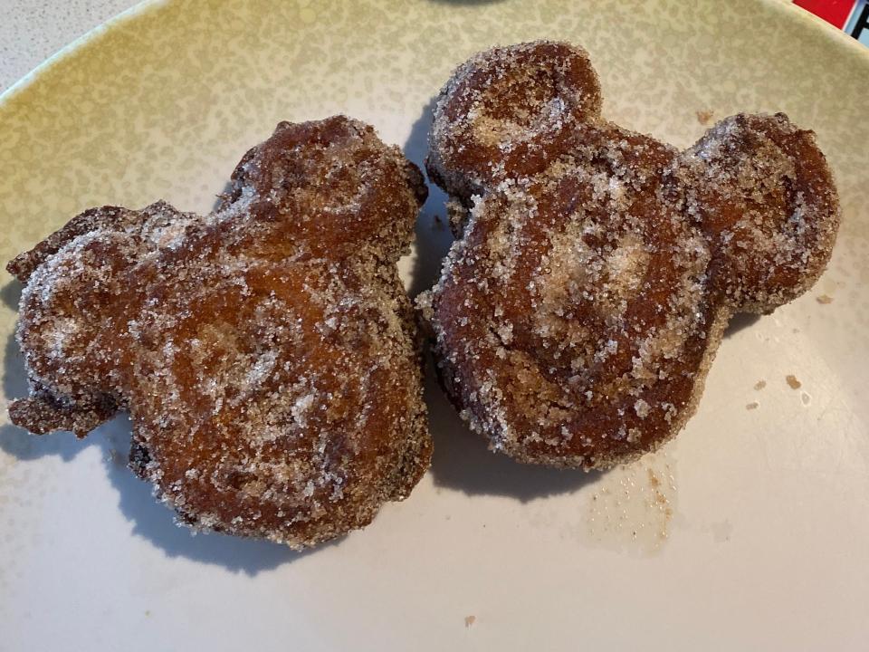 michey-shaped churro waffles on a plate next to a cup of coffee