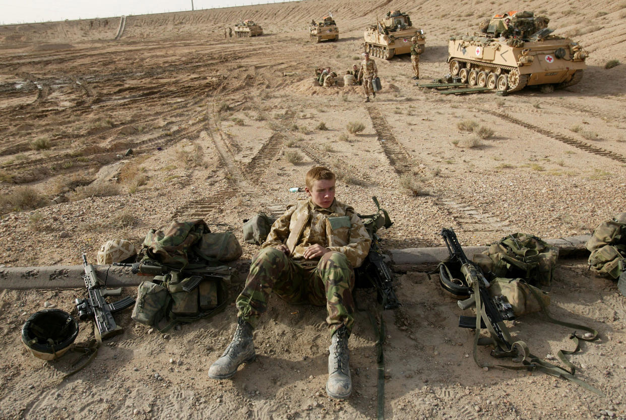 A member of a British tank crew, helmet off, leans against an oil pipeline with his gear arrayed around him. 