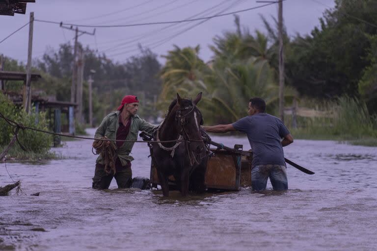 La gente recorre una calle inundada con un carruaje tirado por caballos después del paso del huracán Helene en Guanimar, provincia de Artemisa, Cuba, el miércoles 25 de septiembre de 2024.