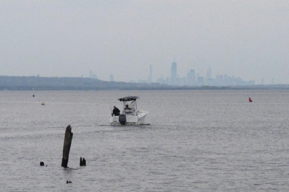 A boat heads out into Raritan Bay in Keyport, N.J., Tuesday, April 19, 2021, with the New York City skyline on the horizon. A Massachusetts company wants to build a high-voltage power line that would come ashore in Keyport and connect electricity from a future wind farm off the New Jersey coast to the onshore electrical grid. (AP Photo/Wayne Parry)