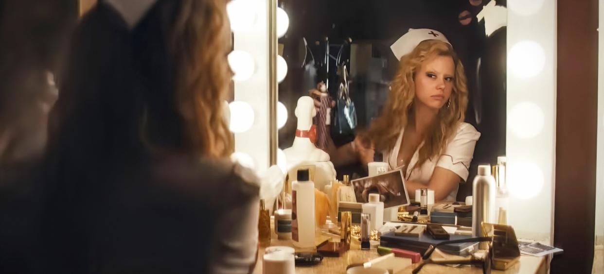 Mia Goth, as adult film actress Maxine Minx in the movie Maxxxine, looks at herself in a dressing room mirror.