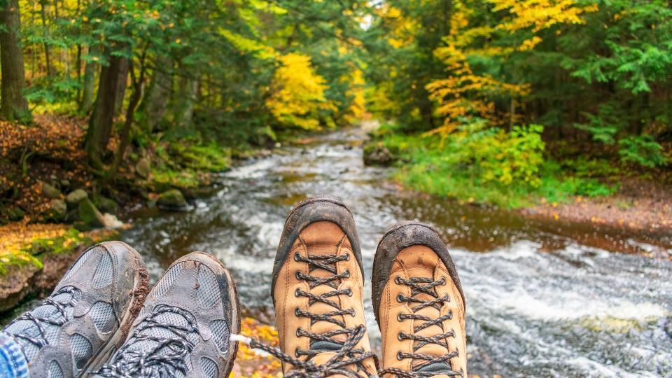 Couple hiking, muddy hiking boots over forest stream in fall stock photo