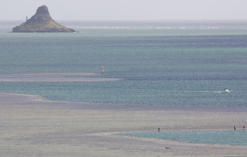 FILE - In this Aug. 15, 2015, file photo, people stand along an area of coral reef near Molokii Island in Hawaii's Kaneohe Bay. Flooding in March 2021 in Hawaii caused widespread and obvious damage. But extreme regional rain events that are predicted to become more common with global warming do not only wreak havoc on land, the runoff from these increasingly severe storms is also threatening Hawaii's coral reefs. (AP Photo/Caleb Jones, File)