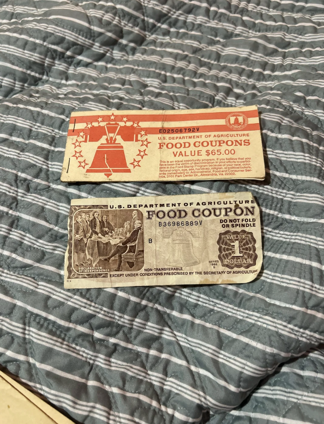 Two U.S. Department of Agriculture food coupon booklets are displayed on a quilt. The top booklet has a value of $65.00