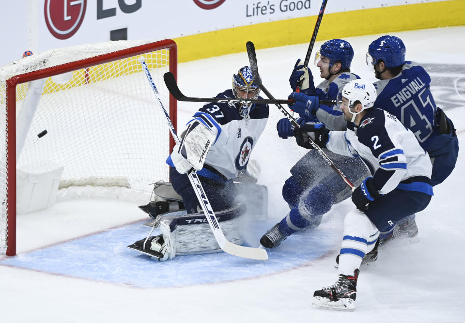 Toronto Maple Leafs left wing Zach Hyman (11) scores past Winnipeg Jets goaltender Connor Hellebuyck (37) as Jets defenseman Dylan DeMelo (2) watches during the first period of an NHL hockey game Tuesday, March 9, 2021, in Toronto. (Nathan Denette/The Canadian Press via AP)