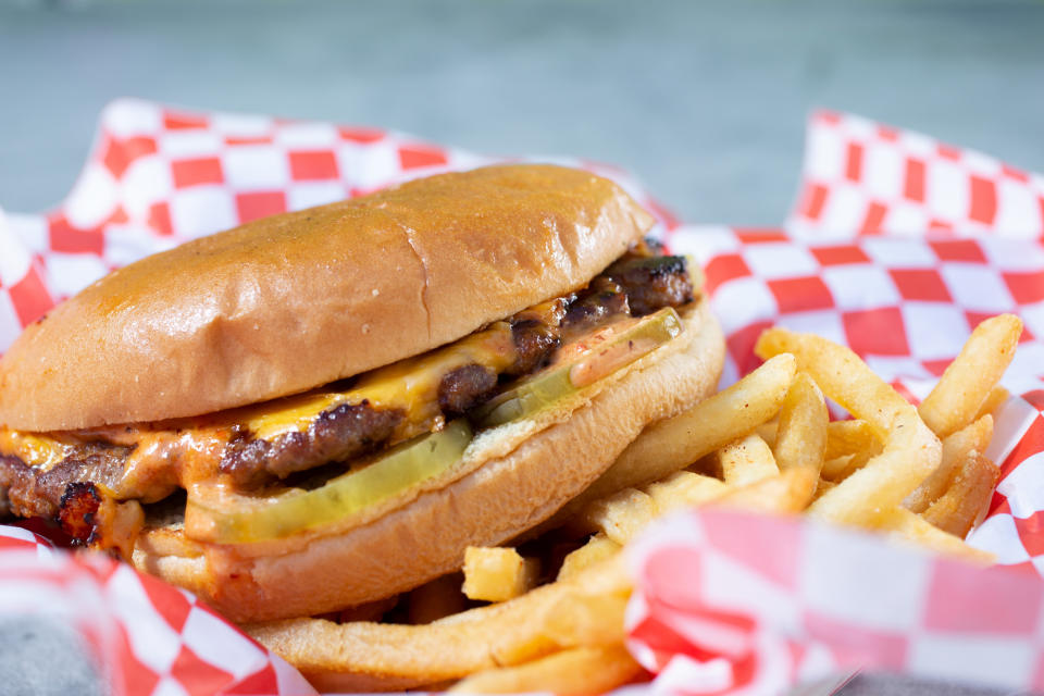 Close-up of a cheeseburger with pickles and fries on a checkered paper