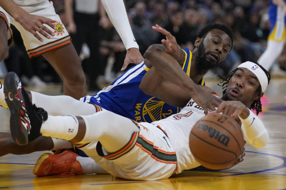 Golden State Warriors forward Andrew Wiggins, rear, and San Antonio Spurs guard Devonte' Graham (4) compete for possession of the ball during the first half of an NBA basketball game Saturday, March 9, 2024, in San Francisco. (AP Photo/Godofredo A. Vásquez)