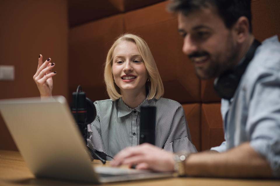 A woman talking into a mic with a man looking at a computer next to her