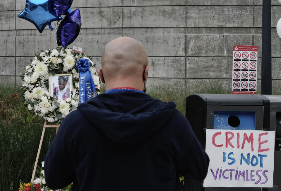 A passerby stops at a memorial for Nurse Sandra Shells at the bus stop on Wednesday, Jan. 19, 2022 in downtown Los Angeles where Shells had been attacked last Thursday. Shells, a 70-year-old nurse, was on her way to work at LA County-USC Medical Center when she was allegedly stabbed, fell backward and hit her head on the ground. She died Sunday, Jan. 16, 2022 at a hospital. (AP Photo/Richard Vogel)