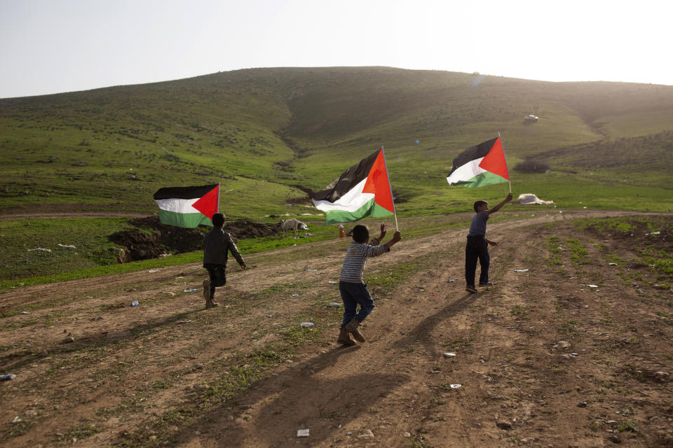 Palestinian Bedouin boys play with Palestinian flags after Israeli troops demolished tents and other structures of the Khirbet Humsu hamlet in the Jordan Valley in the West Bank, Wednesday, Feb. 3, 2021. A battle of wills is underway in the occupied West Bank, where Israel has demolished the herding community of Khirbet Humsu three times in as many months, displacing dozens of Palestinians. Each time they have returned and tried to rebuild, saying they have nowhere else to go. (AP Photo/Maya Alleruzzo)