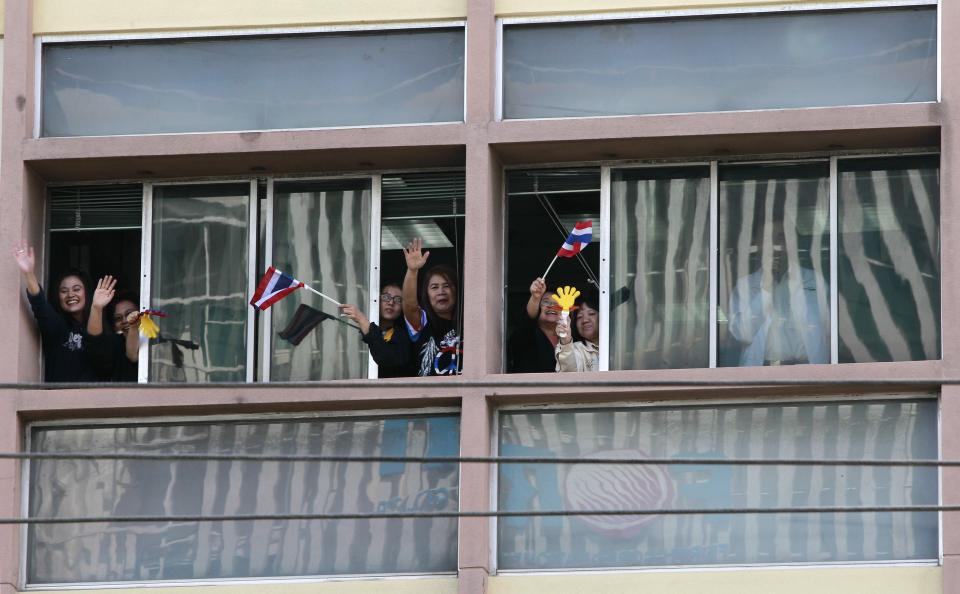 Thai workers wave Thai national flags from a window as anti-government protesters march in a rally in Bangkok January 21, 2014. Some Thai rice farmers have threatened to switch sides and join protesters trying to topple the government if they do not get paid for their crop, a worrying development for Prime Minister Yingluck Shinawatra whose support is based on the rural vote. REUTERS/Chaiwat Subprasom (THAILAND - Tags: POLITICS CIVIL UNREST)