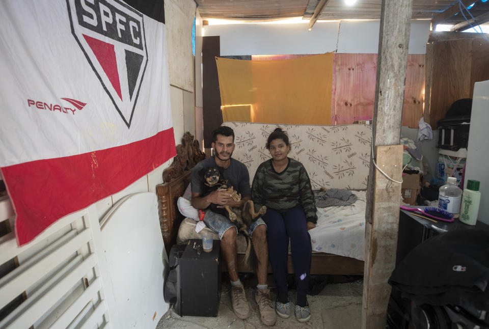 FILE - In this May 15, 2021 file photo, Geovani de Souza, who lost his job as doorman, poses for photos with his wife Juliana Moraes, who is pregnant, inside their home in the Penha Brasil Favela where families have started relocating during the pandemic in Sao Paulo, Brazil. "Without a job, I couldn't pay my rent, was evicted from where I was living and found the solution here," said de Souza, who now relies on occasional work as a bricklayer. (AP Photo/Andre Penner, File)