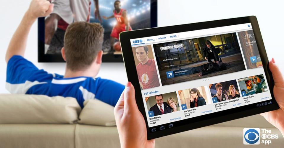 A man sitting on a couch watching basketball, a person holding a tablet with the CBS app in the foreground.