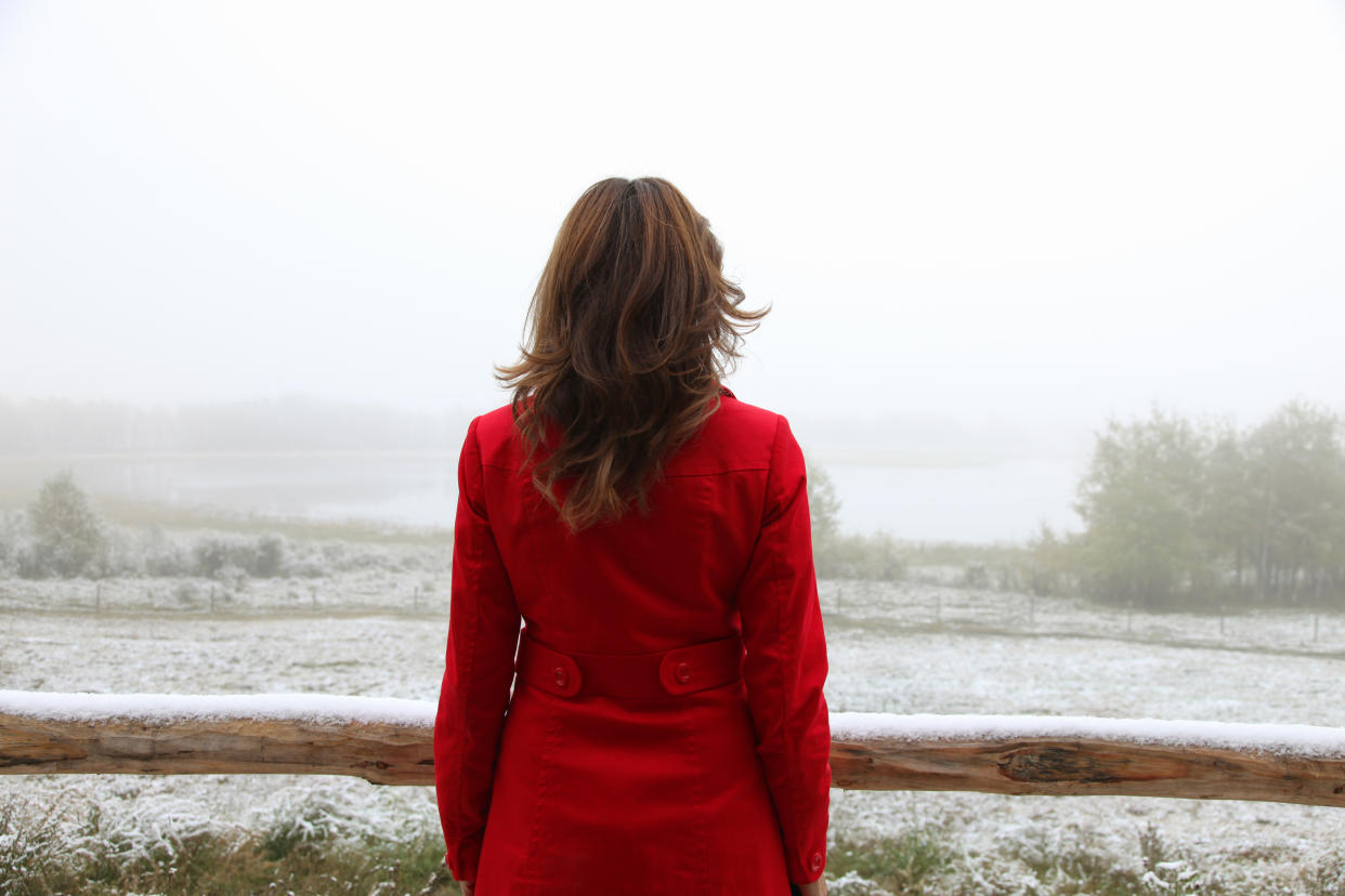 A woman stands in a red coat, over looking a foggy, snow covered landscape.