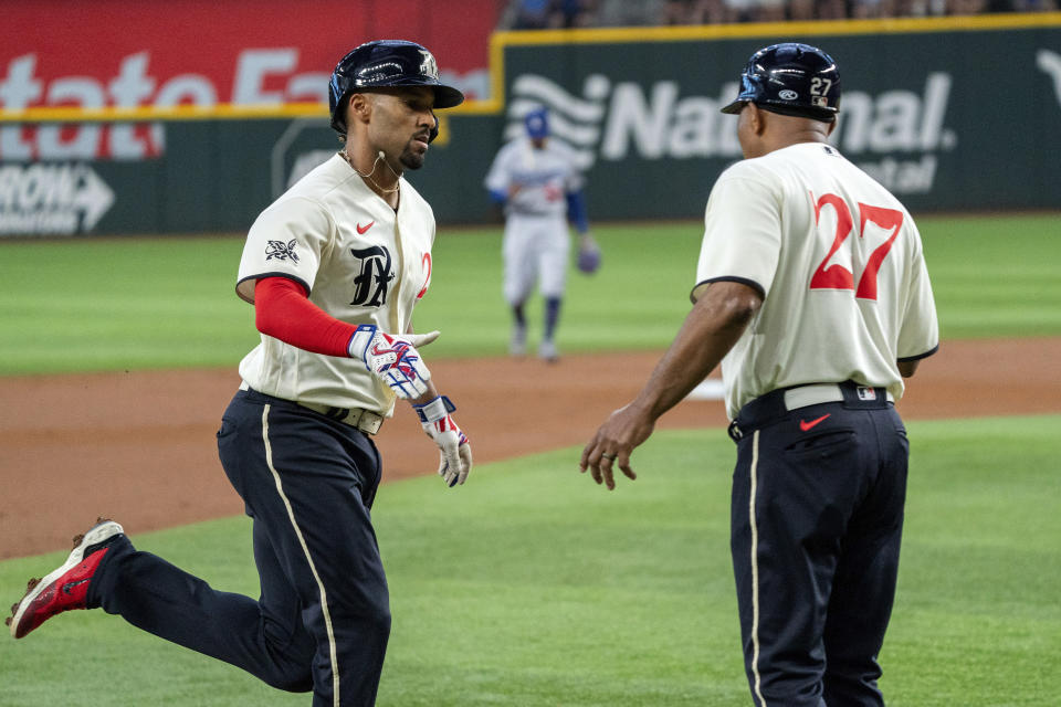 Texas Rangers' Marcus Semien, left, is congratulated by third base coach Tony Beasley, right, after hitting a solo home run off Los Angeles Dodgers starting pitcher Bobby Miller during the first inning of a baseball game Saturday, July 22, 2023, in Arlington, Texas. (AP Photo/Jeffrey McWhorter)