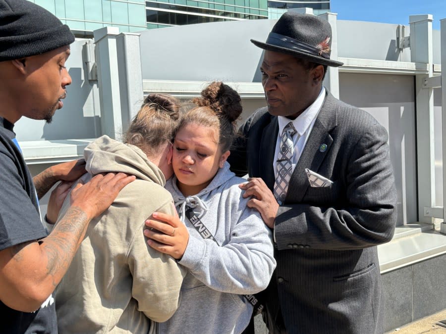 Riley Doggett's mother and sister hug, standing with Jermar Sterling (left), the cousin of Samuel Sterling; and former Kent County Commissioner Robert Womack (right).