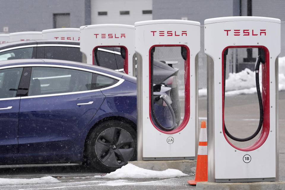 A Tesla electric vehicle, left, sits in a charging station at a dealership, Thursday, Feb. 18, 2021, in Dedham, Mass. After a year of ghostly airports, empty sports stadiums and constant Zoom meetings, growing evidence suggests that the economy is strengthening. Hiring picked up in February 2021. Business restrictions have eased as the pace of viral infections has ebbed. Yet the economy remains far from normal. (AP Photo/Steven Senne)