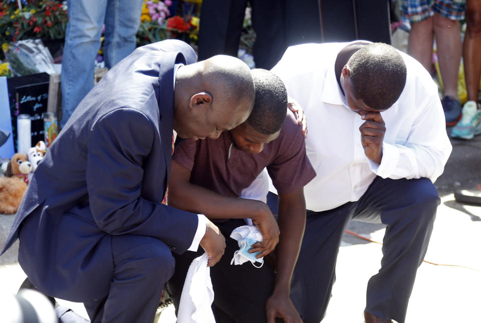 Quincy Mason, center, the son of George Floyd, and family attorney Ben Crump, left, kneel, Wednesday, June 3, 2020 as they visited the site of a memorial in Minneapolis where Floyd was arrested on May 25 and died while in police custody. Video shared online by a bystander showed a white officer kneeling on his neck during his arrest as he pleaded that he couldn't breathe. (AP Photo/Jim Mone)