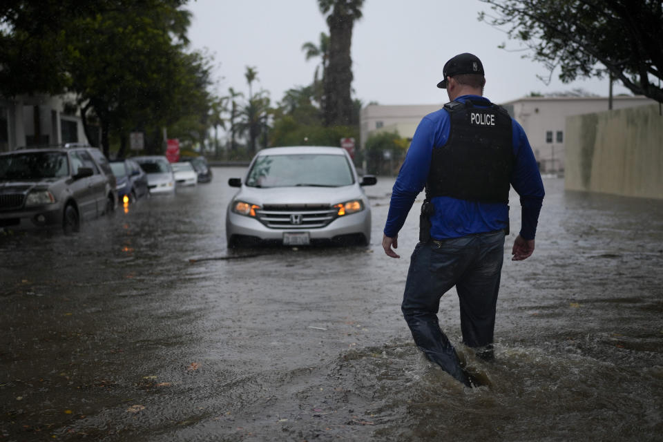 A police officer walks towards a motorist stuck in a flooded street during a rainstorm, Thursday, Dec. 21, 2023, in Santa Barbara, Calif. (AP Photo/Jae C. Hong)