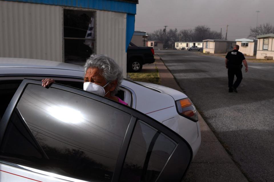 A woman waits for her younger companions to finish retrieving belongings from their home as an Abilene police officer checks on other people evacuating the Continental Villa mobile home park. A quickly-moving grass fire west of town was closing on the park, forcing the evacuation.