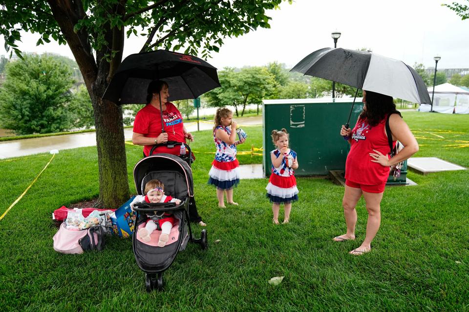 Stephanie Harvey, 28, of Hillitop, at right, stands with her daughters, Mary Henry, 4, Leah Henry, 9, Savannah Harvey, 11 months old, and mother-in-law Vickie Bruce, 53, while waiting out the rain under a tree with their umbrellas for Monday's Red, White & Boom festivities in Downtown Columbus.