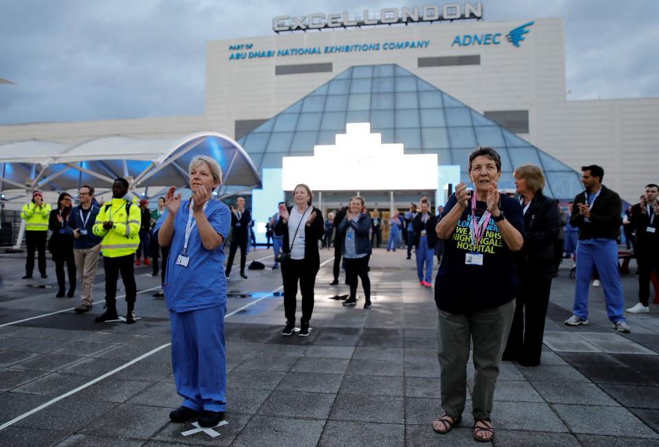 Medical staff and workers take part in a national "clap for carers" to show thanks for the work of Britain's NHS (National Health Service) workers and other frontline medical staff around the country as they battle with the novel coronavirus pandemic, outside of the ExCeL London exhibition centre, which has been transformed into the "NHS Nightingale" field hospital in London on April 30, 2020. - Britain is "past the peak" of its coronavirus outbreak, Prime Minister Boris Johnson said Thursday, despite recording another 674 deaths in the last 24 hours, taking the toll to 26,711. "For the first time, we are past the peak of this disease... and we are on the downward slope," Johnson said in his first media briefing since returning to work following his own fight against the virus. (Photo by Tolga AKMEN / AFP) (Photo by TOLGA AKMEN/AFP via Getty Images)