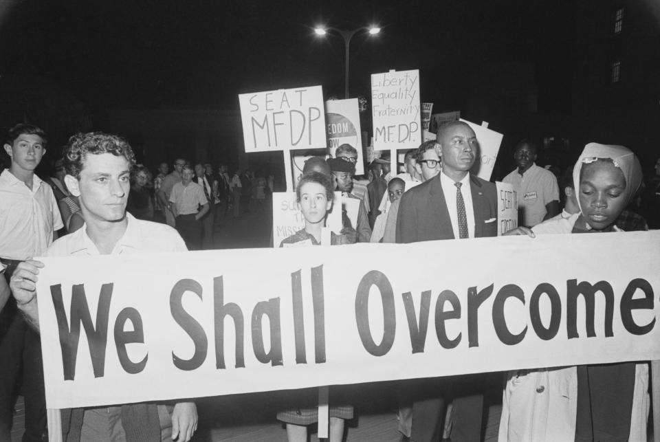 a 1960s protest with a sign saying "we shall overcome"