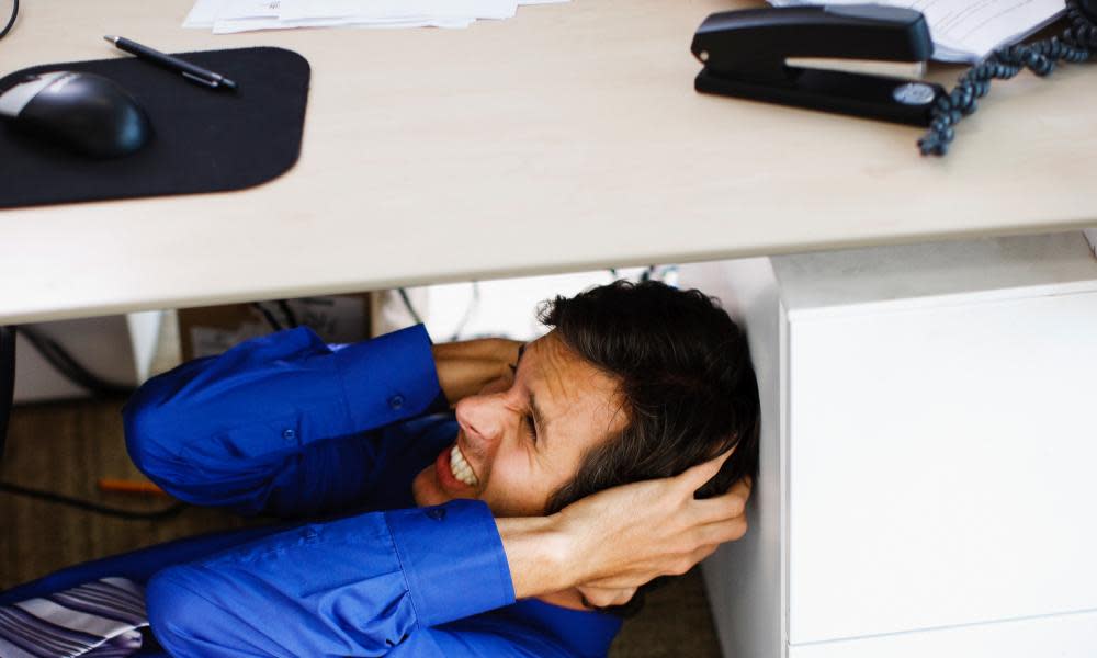 Frustrated businessman covering ears under desk