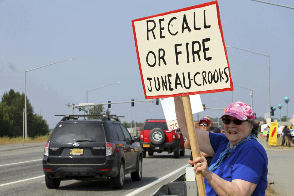 Laura Jones holds a protest sign Monday, July 8, 2019, in Wasilla, Alaska. Some Alaska lawmakers are meeting in Wasilla July 8 instead of Juneau, where state House and Senate leadership have decided to hold the special session. (AP Photo/Mark Thiessen)