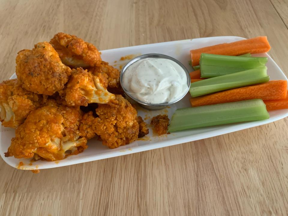 buffalo cauliflower bites on white plate with dip, celery, and carrots