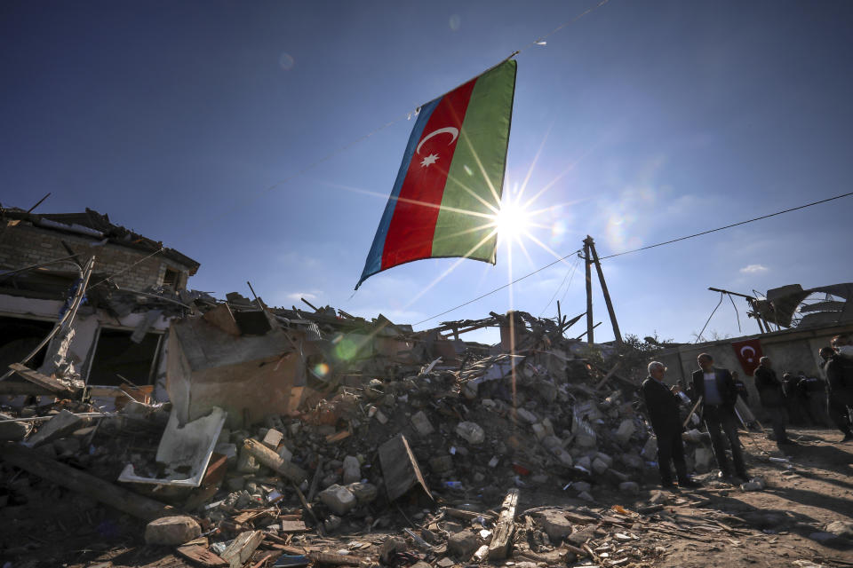 Azerbaijan's national flag flies over destroyed houses in a residential area that was hit by rocket fire overnight by Armenian forces, on Thursday, Oct. 22, 2020 in Ganja, Azerbaijan's second largest city, near the border with Armenia. Heavy fighting over Nagorno-Karabakh is continuing with Armenia and Azerbaijan trading blame for new attacks. The nearly four weeks of hostilities have raised the threat of Turkey and Russia being drawn into the conflict. (AP Photo/Aziz Karimov)