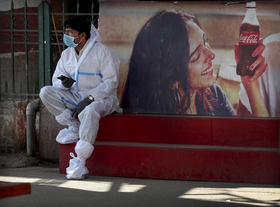 A health worker wearing personal protective equipment takes a break as he awaits travelers to arrive outside a a train station in Bengaluru, India, Monday, Feb. 22, 2021. Cases of COVID-19 are increasing in some parts of India after months of a steady nationwide decline, prompting authorities to impose lockdowns and other virus restrictions. (AP Photo/Aijaz Rahi)