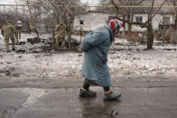 An elderly lady walks by as members of the Joint Centre for Control and Coordination on ceasefire of the demarcation line, or JCCC, survey a crater and damage to a house from artillery shell that landed in Vrubivka, one of the at least eight that hit the village today, according to local officials, in the Luhansk region, eastern Ukraine, Thursday, Feb. 17, 2022. U.S. President Joe Biden warned that Russia could still invade Ukraine within days and Russia expelled the No. 2 diplomat at the U.S. Embassy in Moscow, as tensions flared anew in the worst East-West standoff in decades. (AP Photo/Vadim Ghirda)