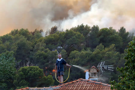 A man waters the roof of his house with a garden hose as a smoke from a burning wildfire fills the sky in Carros, near Nice, France. REUTERS/Eric Gaillard