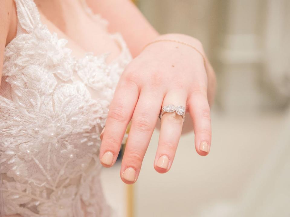 A woman in a wedding dress holds her hand up with an engagement ring on it.