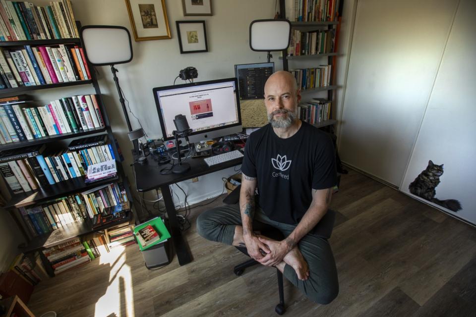 Derek Beres sits in lotus position on a desk chair in his office.